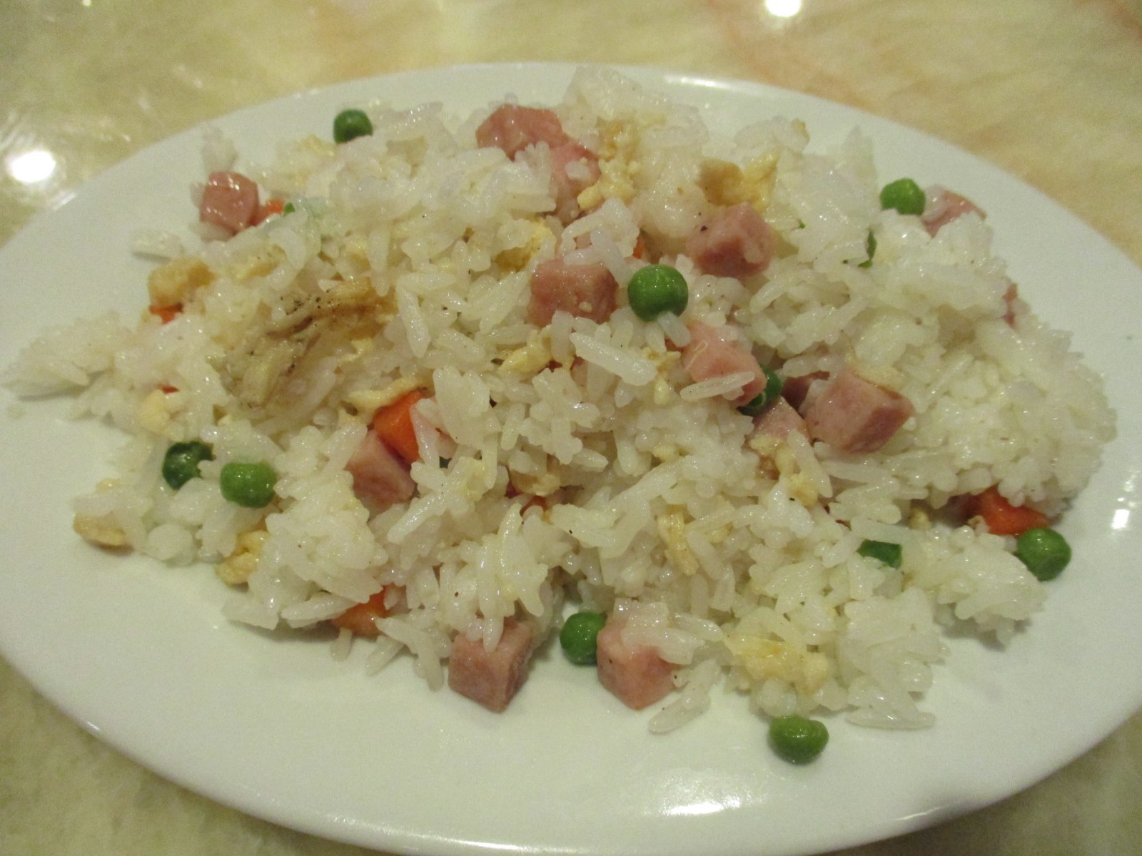 Plato de arroz frito con dados de jamón, guisantes, zanahoria y tortilla sobre una mesa de restaurante