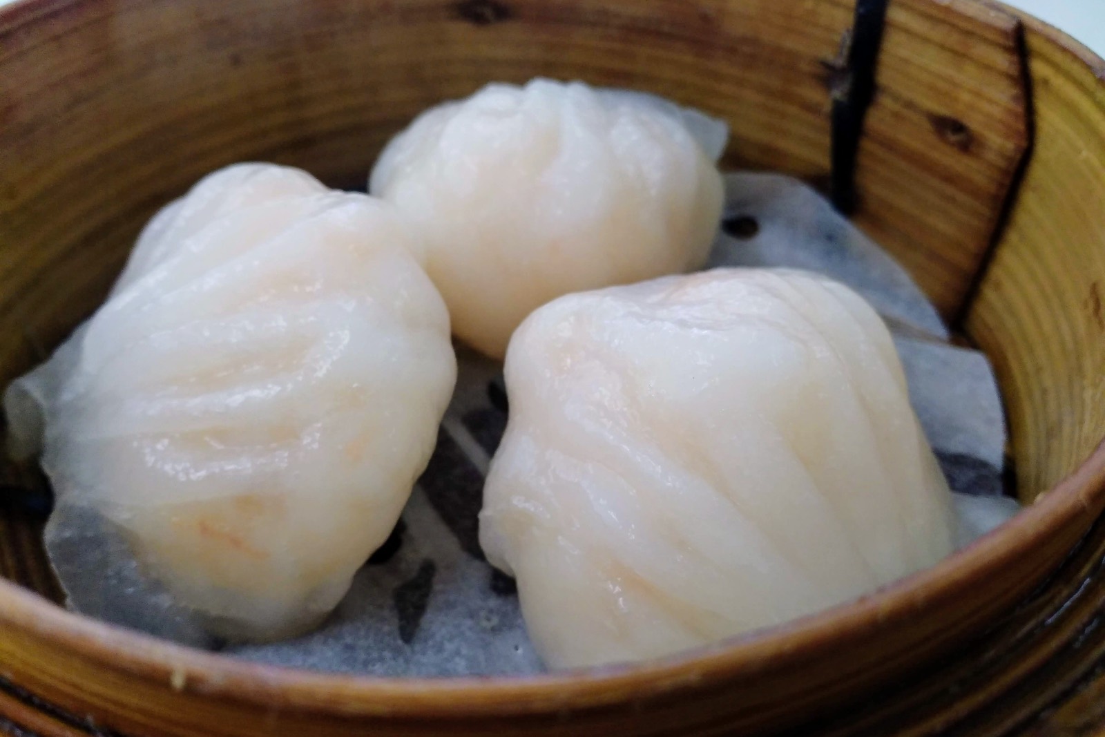 Tres empanadillas de gamba har gow, de masa translúcida y plisada, en una vaporera de bambú