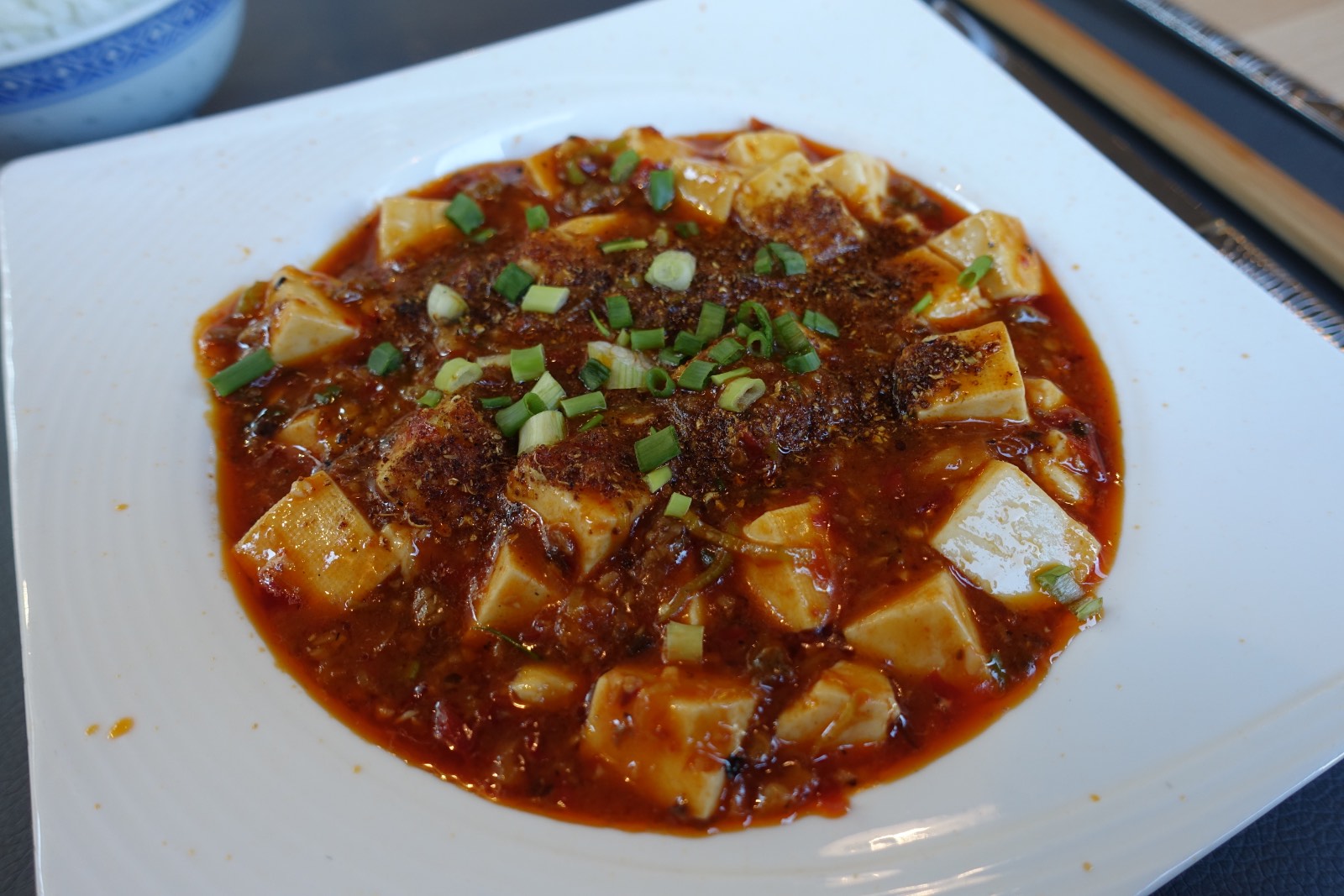 Mapo tofu: dados de tofu en salsa roja de guindilla con carne picada y cebolleta, en un plato blanco